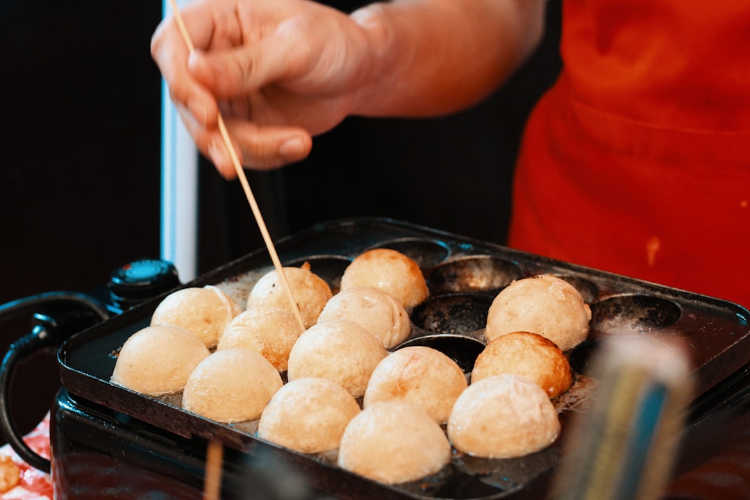 A vibrant image of a Takoyaki maker filled with cooking octopus balls, surrounded by dipping sauces 