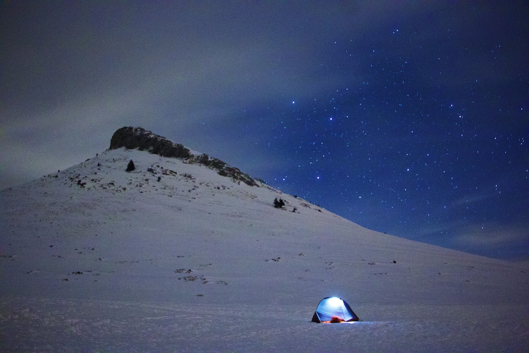 Product shot of the Snow Peak Takibi Lantern in use at a campsite, showcasing its aluminum and glass