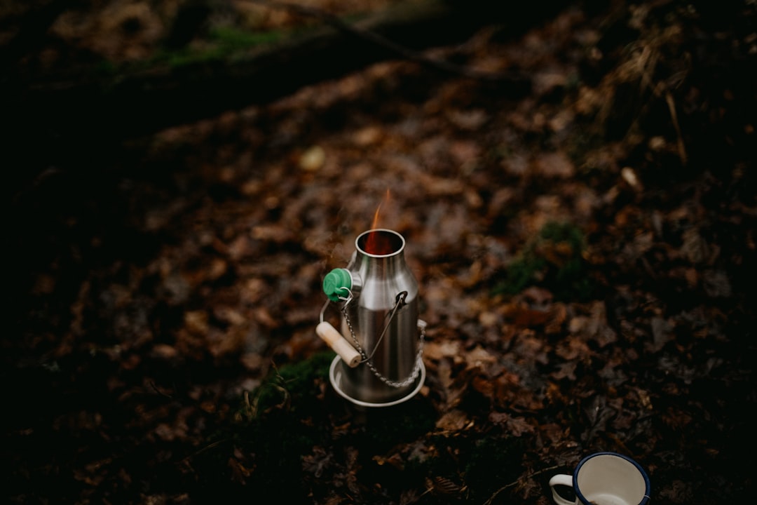 An outdoor scene featuring the Snow Peak Ti-Solid Kettle being used in a camping setup.