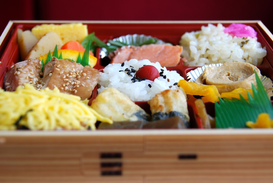A beautifully arranged bento box featuring a variety of colorful foods like rice, grilled chicken, c