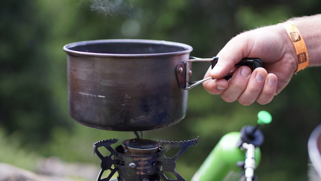 Photo of a camper repairing or maintaining a camping stove, showing close-up hands changing a jet or