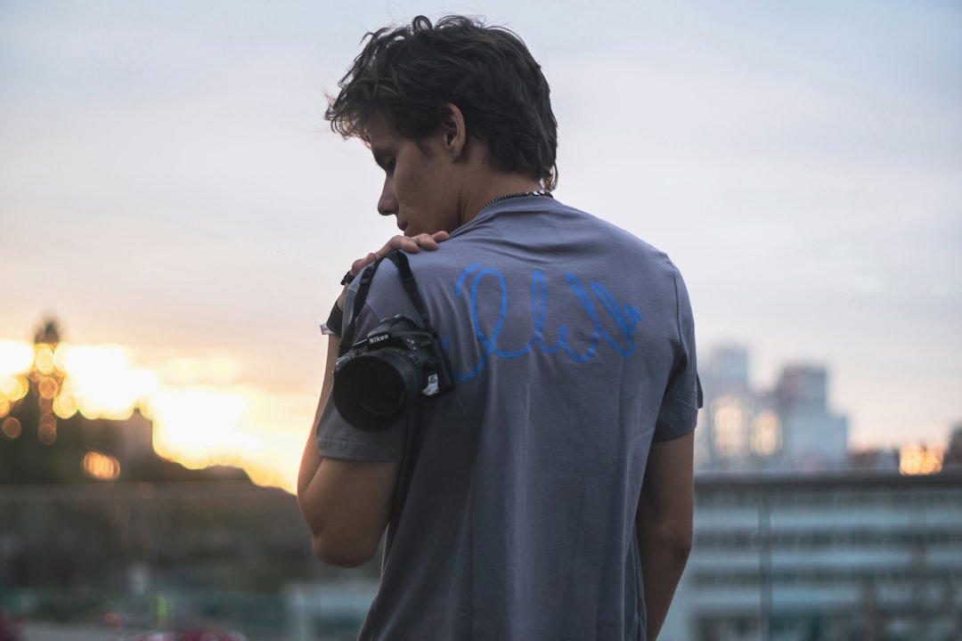 A travel photographer holding a Panasonic Lumix mirrorless camera while standing against a scenic Am