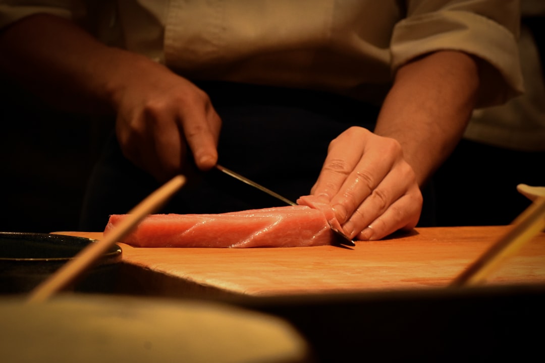 A detailed shot of the Yoshihiro Blue Steel No.2 Yanagiba Sushi Knife slicing fresh sashimi on a tra